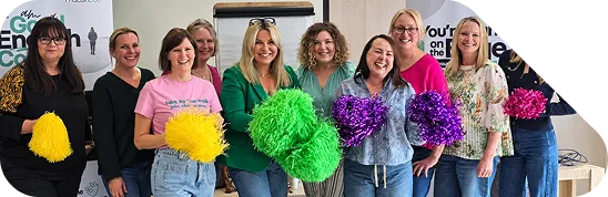 The Paseda team smiling together holding colourful pom-poms